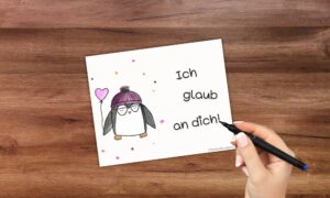 Brotboxkarte mit handgemaltem süßen Pinguin und einer Hand, die "Ich glaub an dich" schreibt